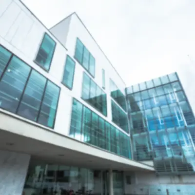 A modern, angular building with large glass windows reflecting a cloudy sky and surrounded by greenery A modern, angular building with large glass windows reflecting a cloudy sky and surrounded by greenery